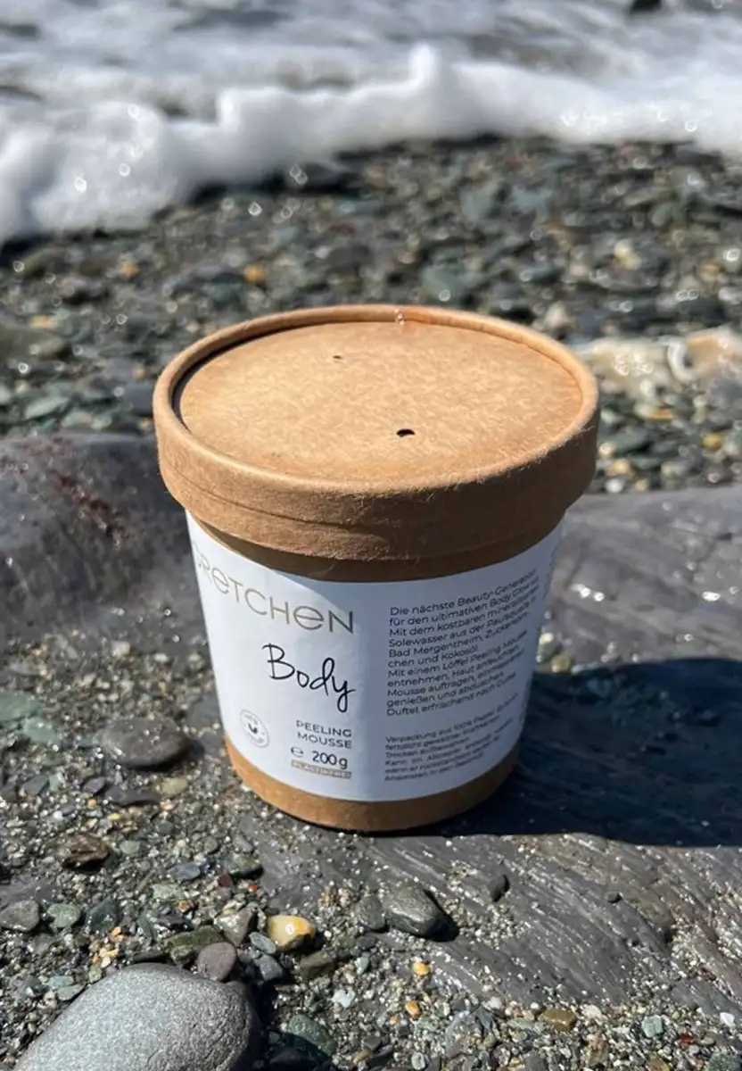 Gretchen Body Peeling Mousse in a kraft carton on a pebble beach – body scrub with brine and sugar granules